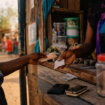 Woman completing a mobile money transaction at a rural market stall in Kenya, illustrating fintech-driven global financial inclusion