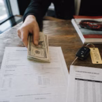 Hand placing cash down payment on an auto loan contract at a dealership desk