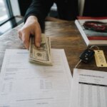 Hand placing cash down payment on an auto loan contract at a dealership desk