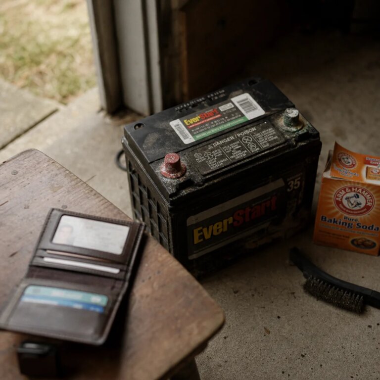 Car battery with corroded terminals on a garage floor with cleaning tools nearby